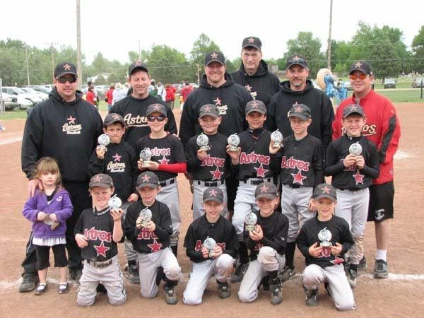 Youth baseball team posing together on a field with coaches, wearing matching black and red uniforms.