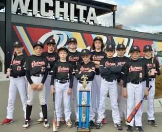 Youth baseball team posing with trophy in front of Wichita sign, wearing black uniforms with white pants.