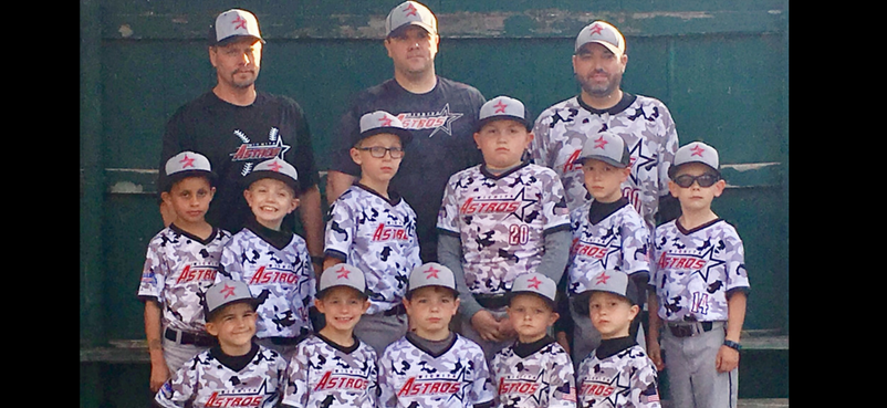 Youth baseball team and coaches posing in uniform on a field, with a green fence behind them.