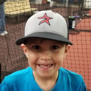 Smiling child in a gray baseball cap and blue shirt at a baseball field