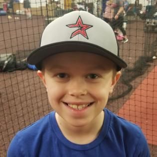 Smiling child in a gray cap and blue shirt in an indoor sports net area