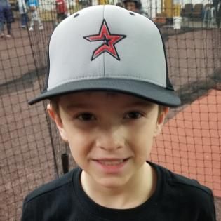Child wearing a gray cap with a red star, smiling on a baseball field