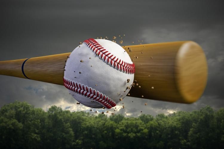 Baseball colliding with a wooden bat above a cloudy green field