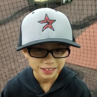 Child wearing glasses and a gray cap with a red star, smiling on a sports court.