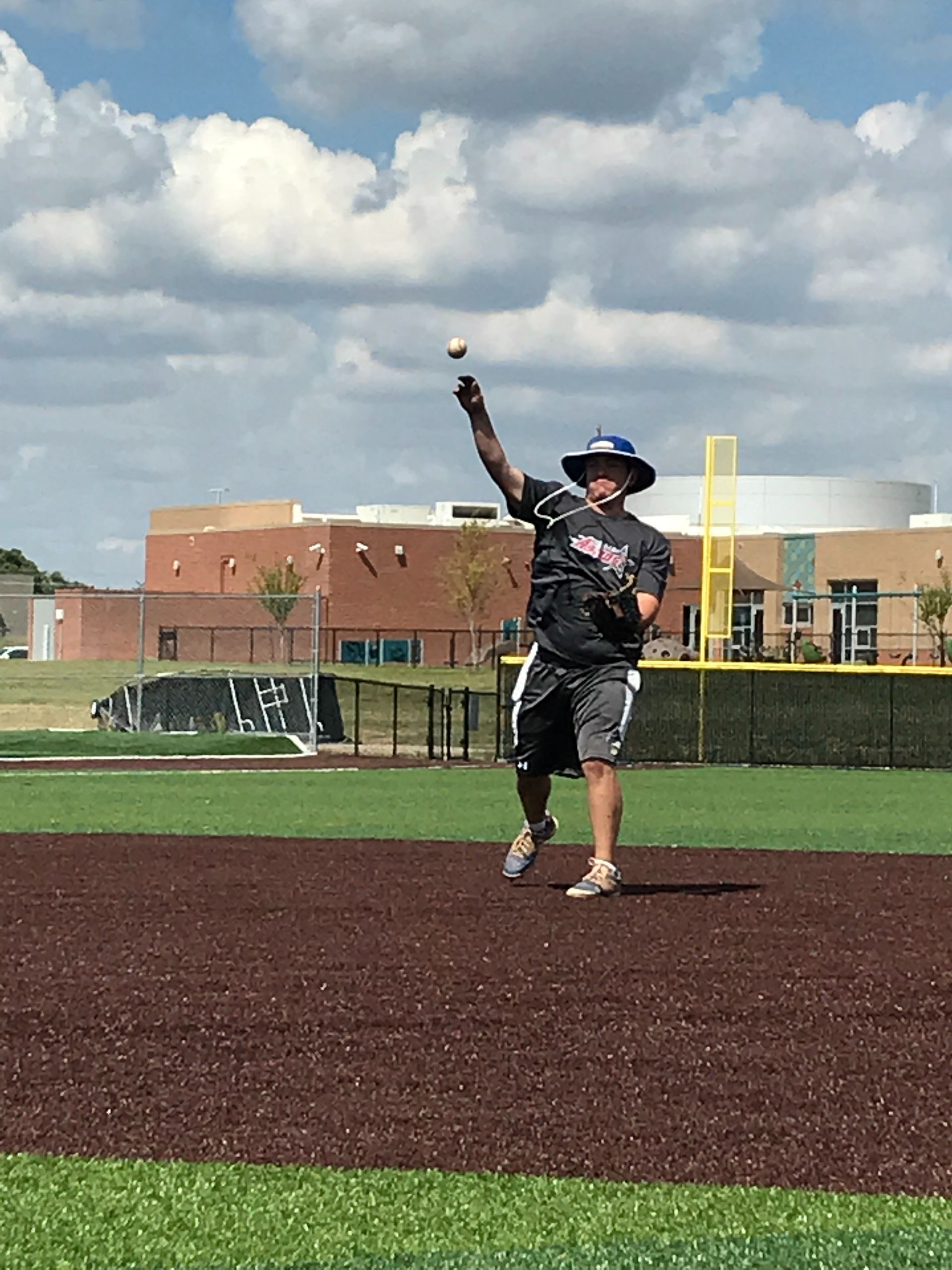Softball pitcher in black uniform mid-throw on a field under a cloudy sky