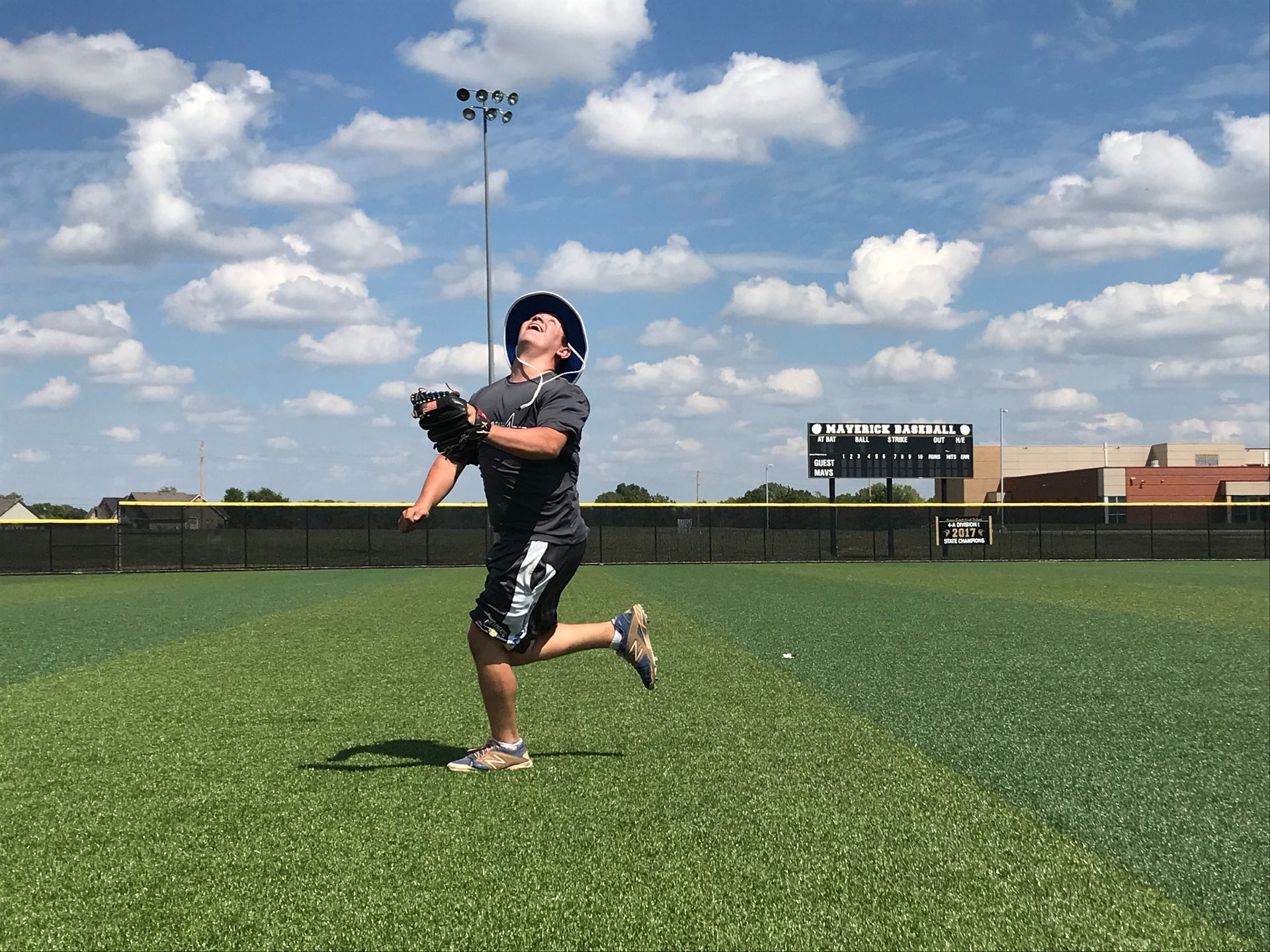 Baseball player in black uniform catching a ball on a green field under a blue sky