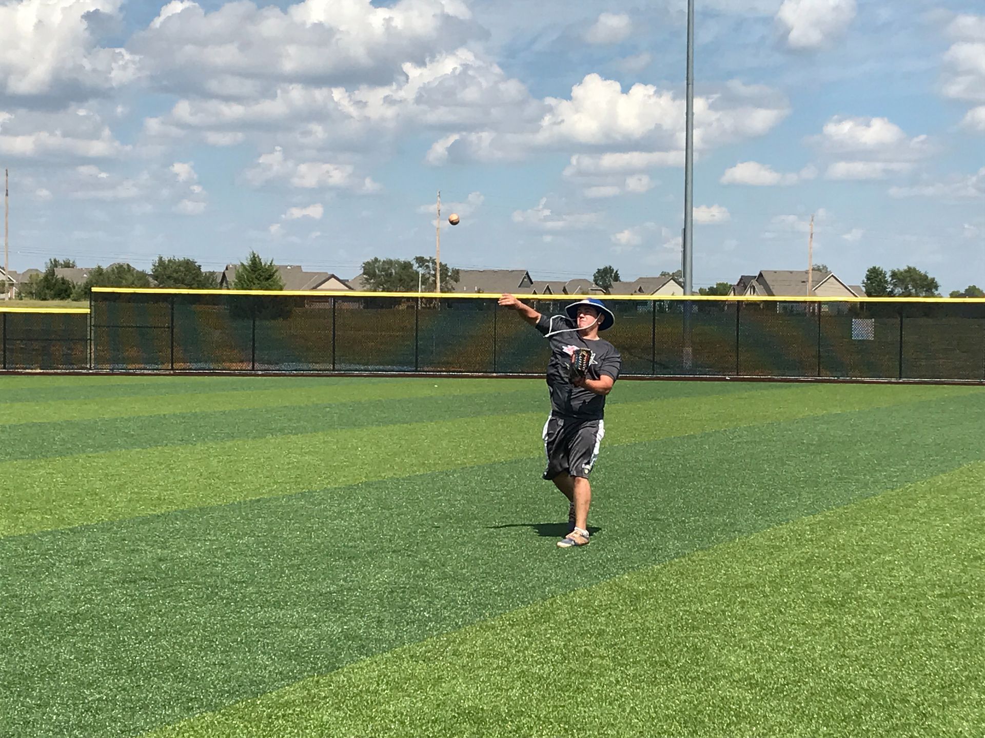Person standing on a baseball field, catching a ball with a glove under a cloudy sky.