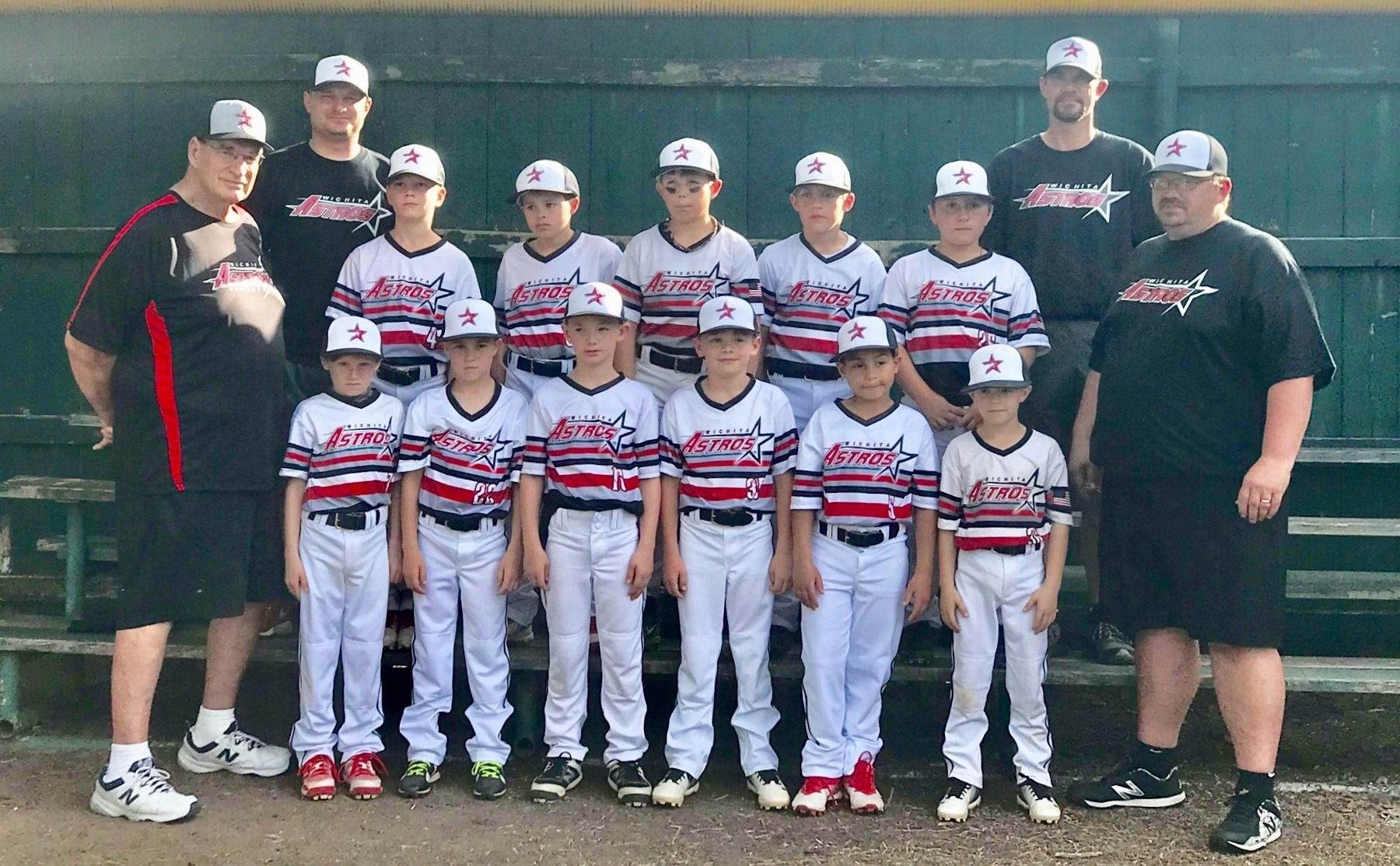 Youth baseball team and coaches posing in uniform in front of a dugout