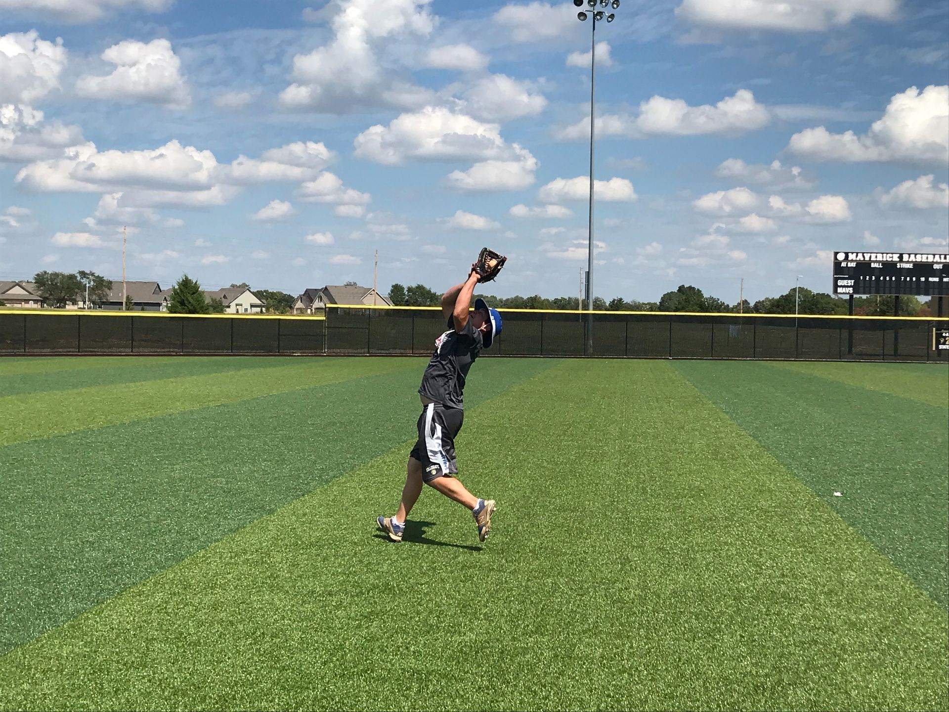 Baseball player catching a ball on a green field under a cloudy sky