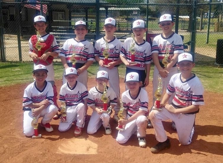 Youth baseball team posing in white and maroon uniforms on a dirt field, holding a trophy.
