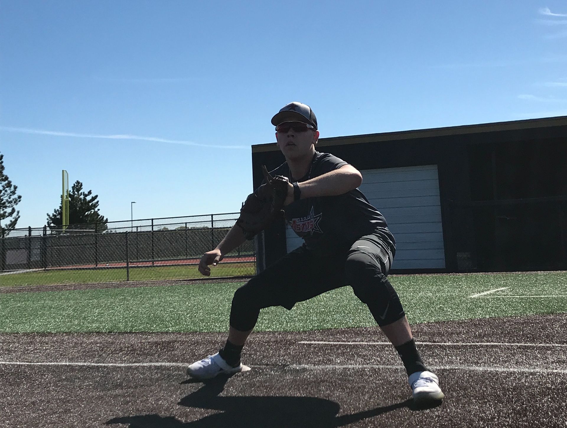 Athlete crouched on a turf field in a ready stance, wearing black gear and white shoes.