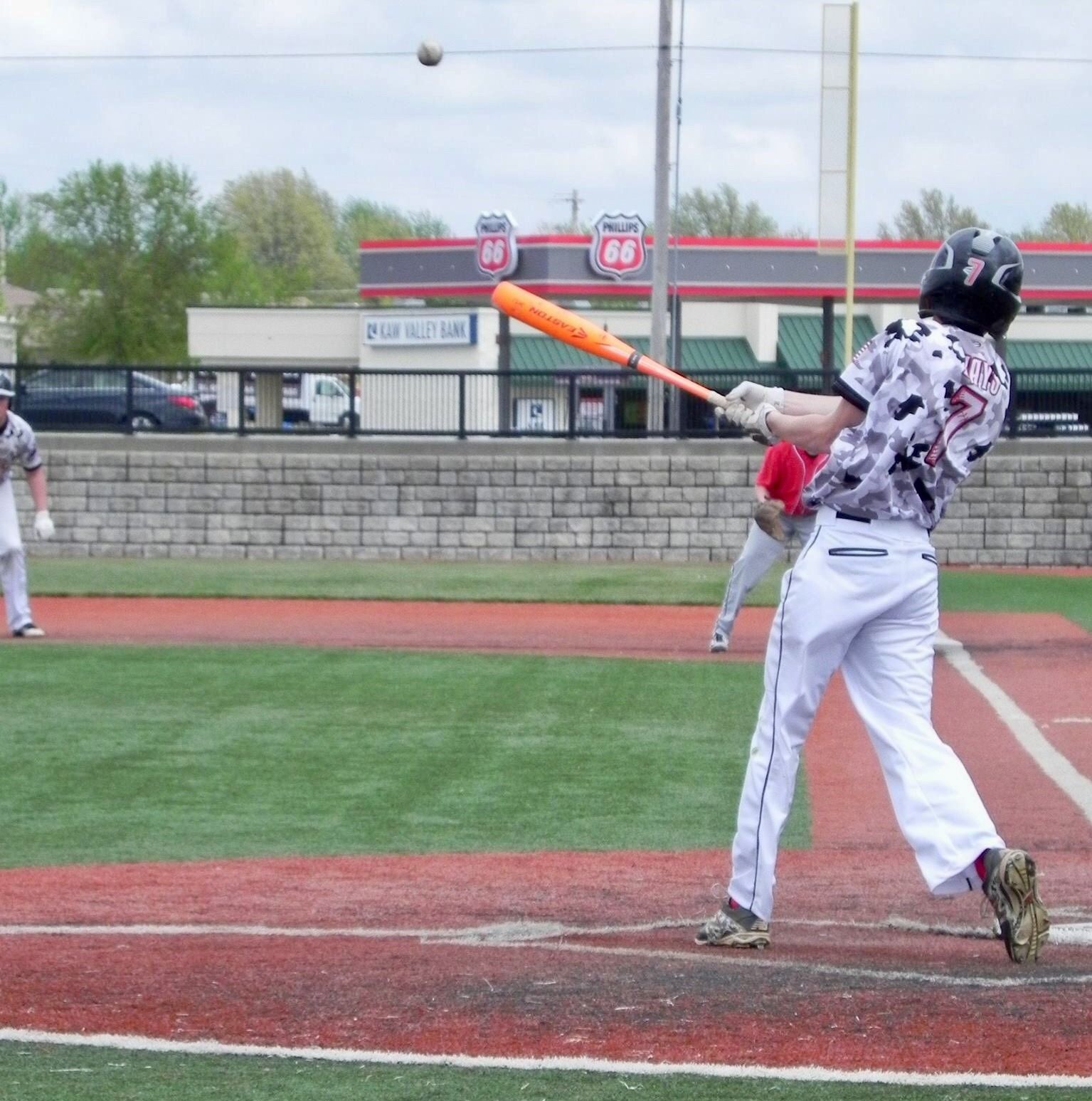 Baseball batter in white swings at a pitch on a field, with a ball visible overhead.