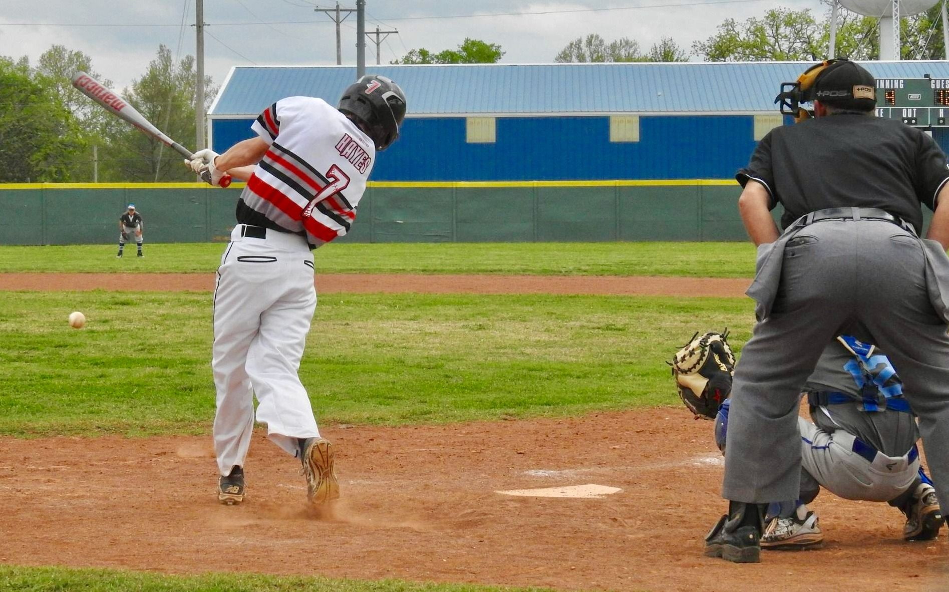 Baseball batter swinging at home plate while catcher and umpire watch on a dirt field
