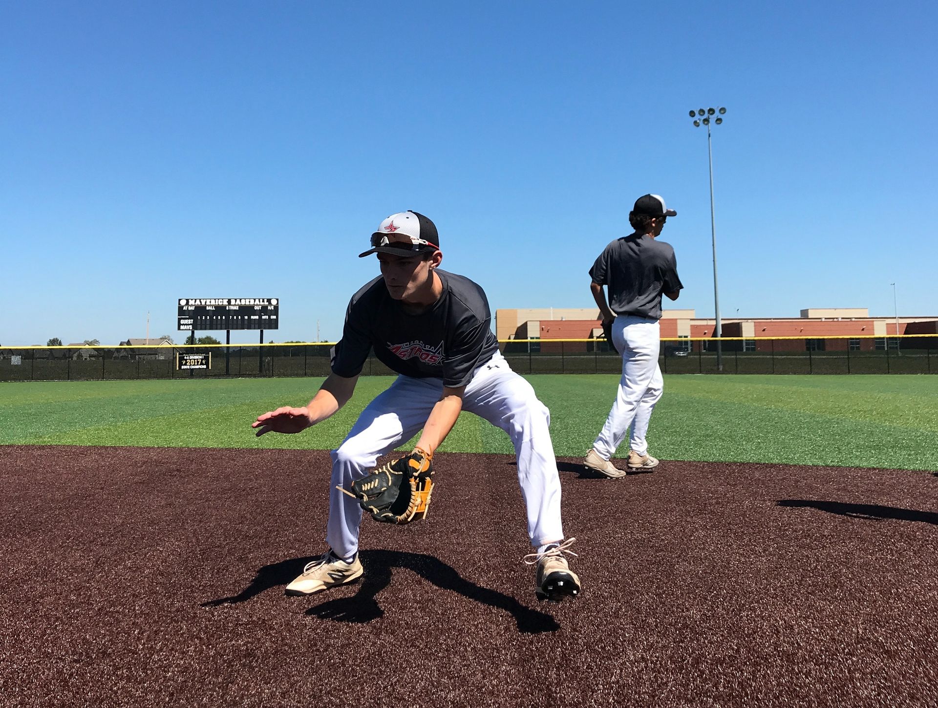 Baseball players fielding a ground ball on a sunny field, one crouched in the foreground