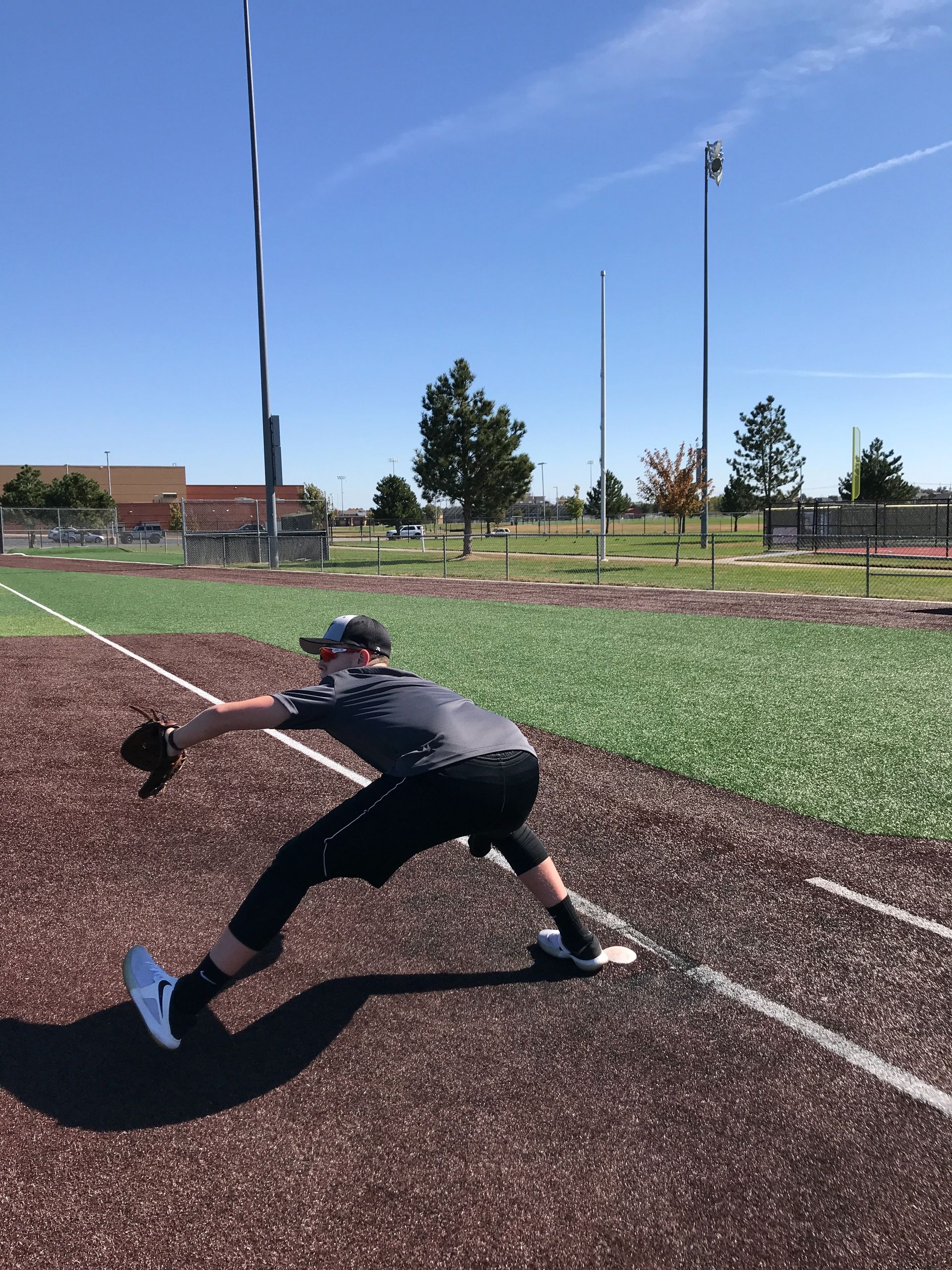 Baseball player stretching on a field, reaching low with glove near the foul line.