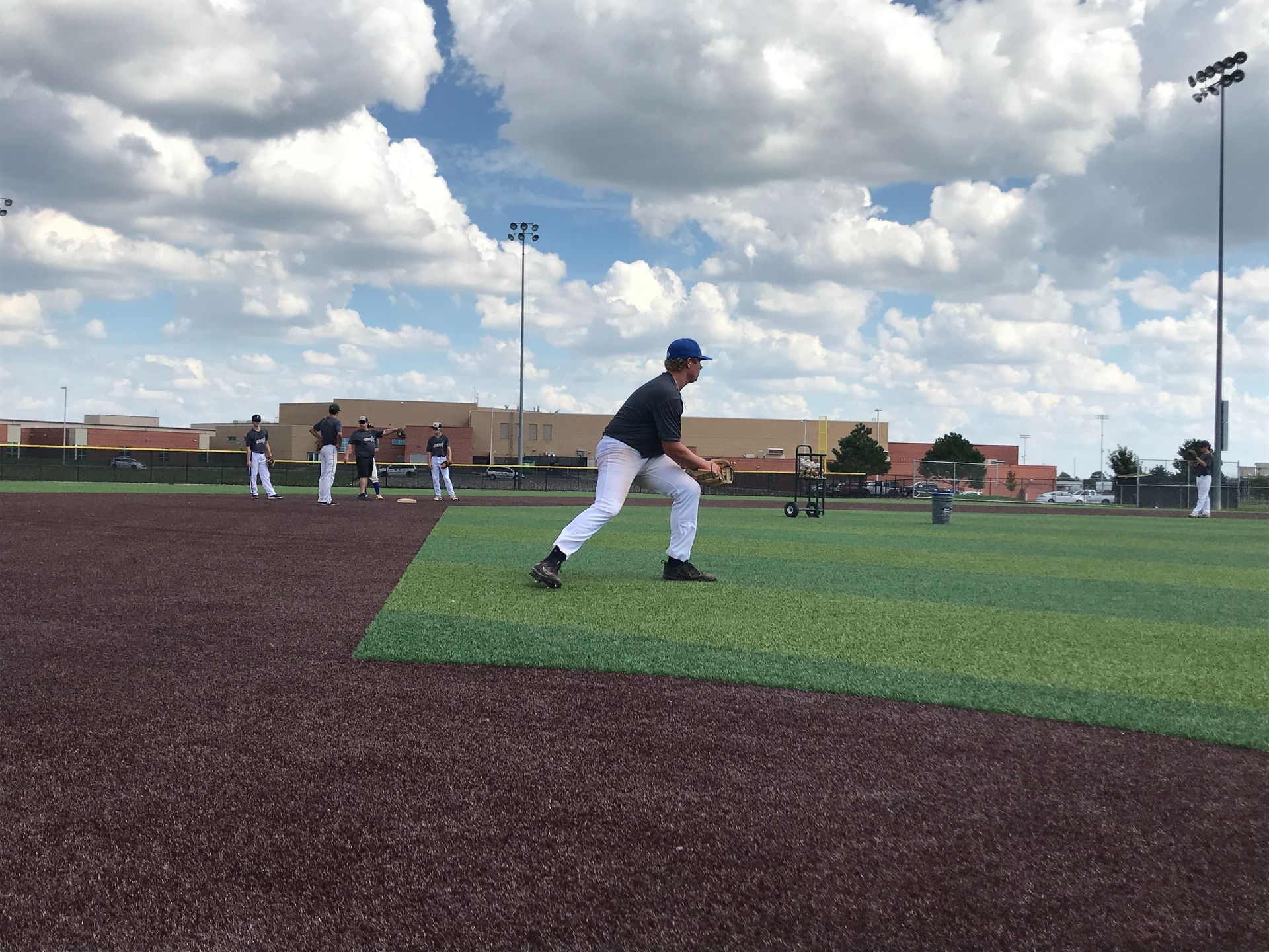 Youth baseball player fielding a grounder on an artificial turf field under a cloudy sky