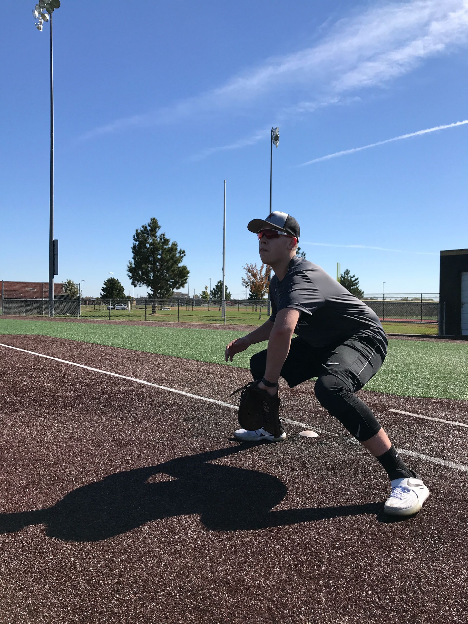 Baseball player crouched on a field in sunlight, ready to catch a ground ball.