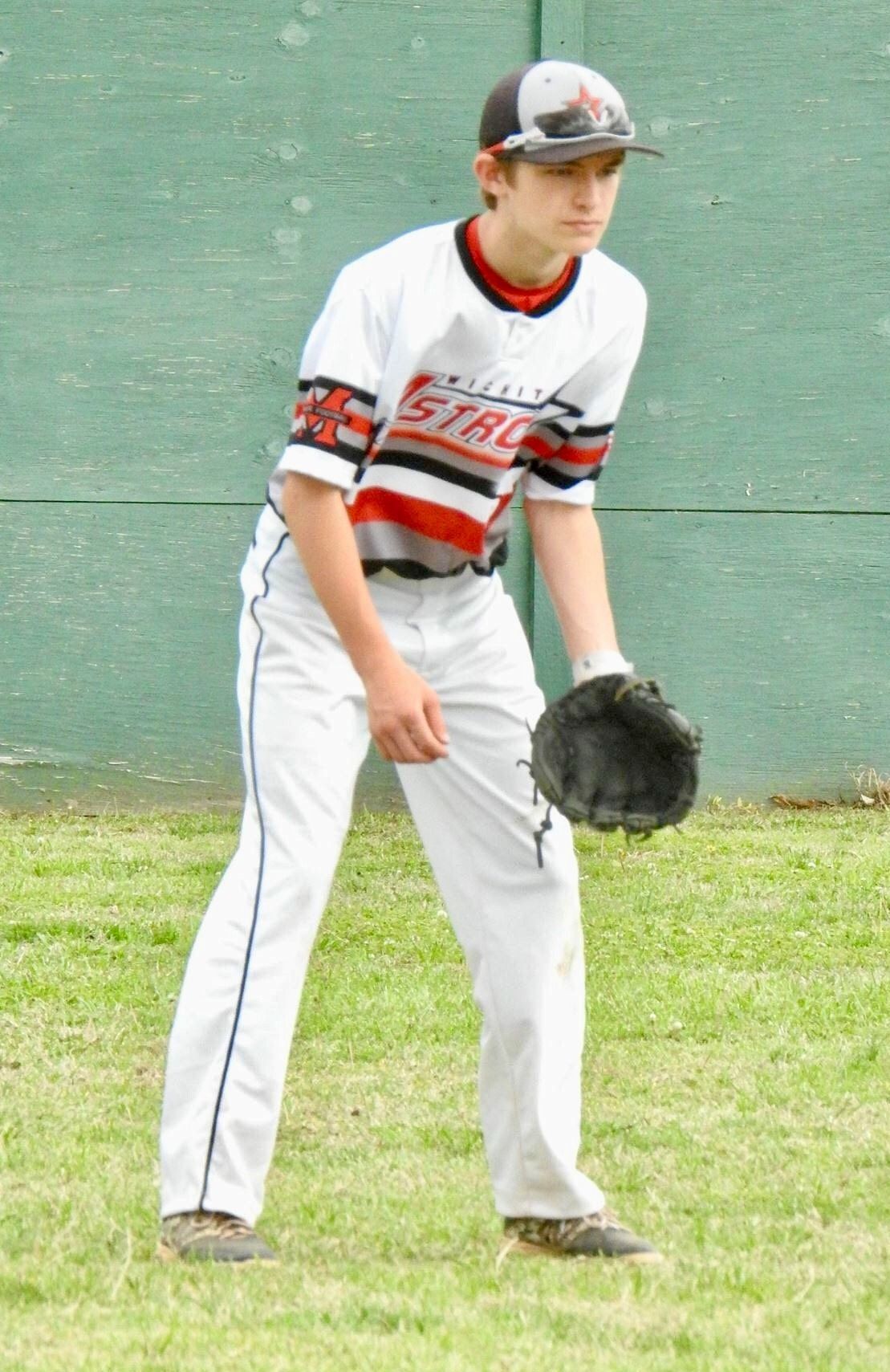 Baseball player in white and red uniform fielding a ball on grass near a green outfield wall