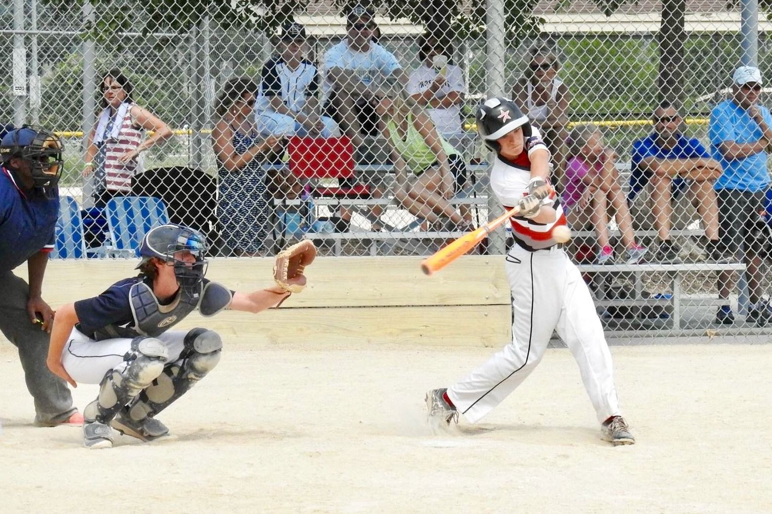 Baseball batter in white swings at a pitch while catcher crouches behind the plate on a sunny field.