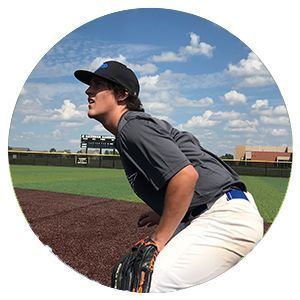 Baseball player in gray uniform crouches on field under a cloudy sky
