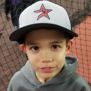 Young child in a white cap with a red star, standing in front of a netted sports background.
