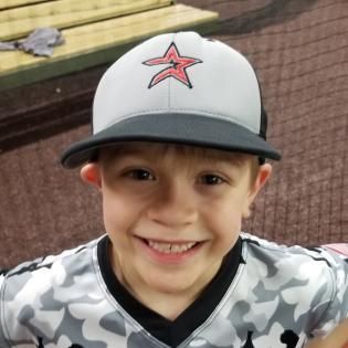 Smiling child in a white baseball cap and gray camo sports jersey indoors