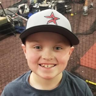 Smiling child in a white-and-black cap standing in a batting cage
