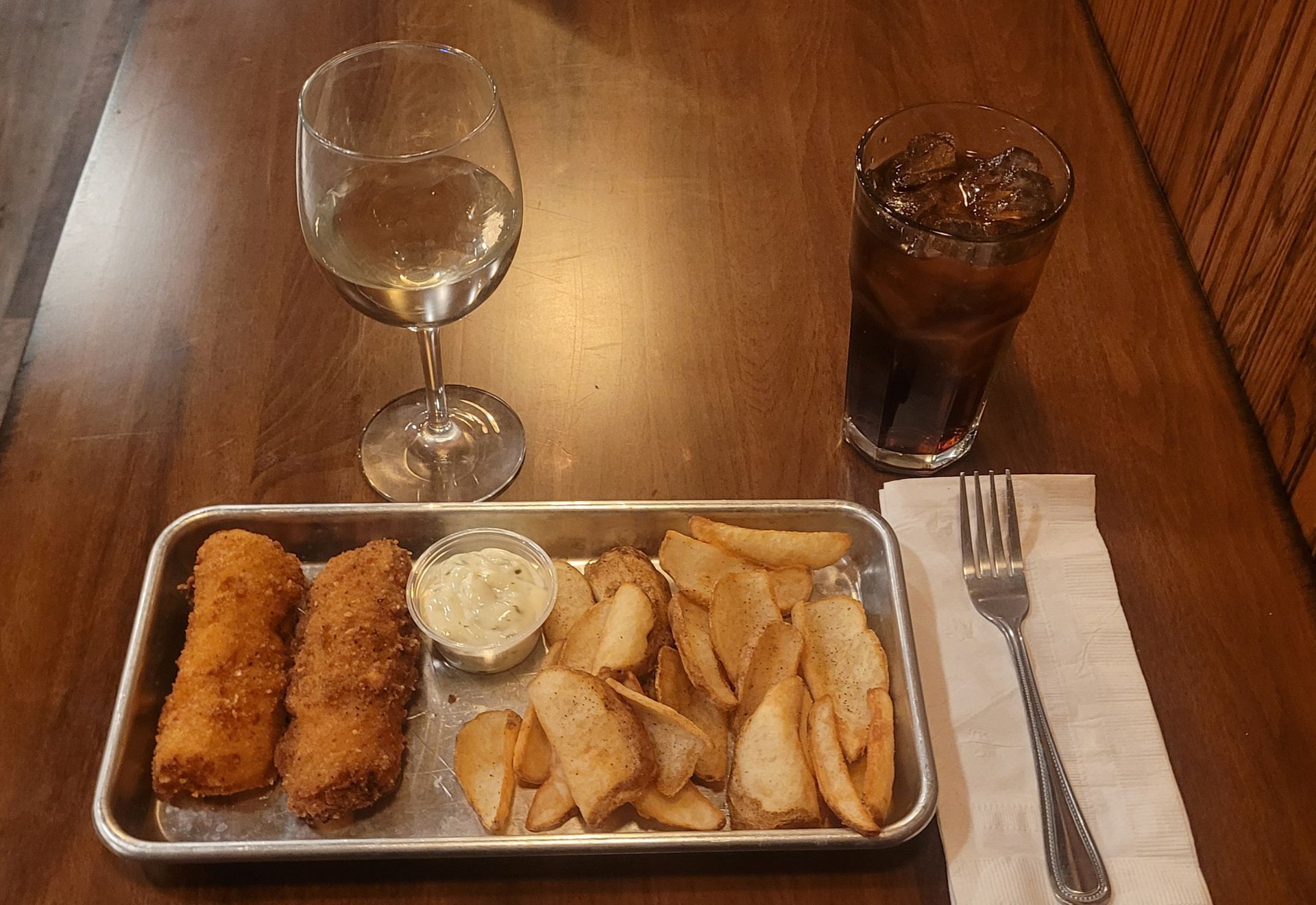 Tray of fried appetizers and dipping sauce on a restaurant table with a wine glass and iced drink