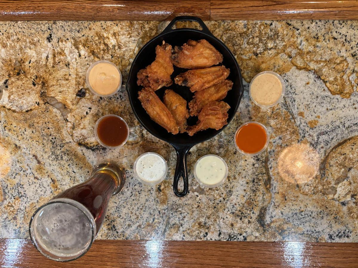 Overhead view of fried chicken in a skillet, surrounded by dipping sauces on a granite counter