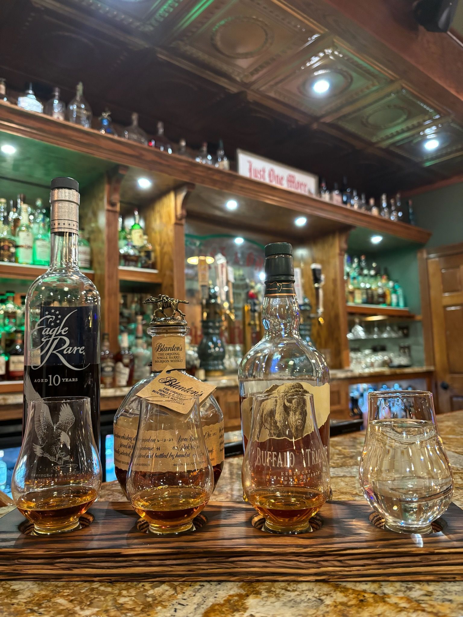 Assorted glass liquor bottles on a wooden bar counter in a warmly lit pub interior