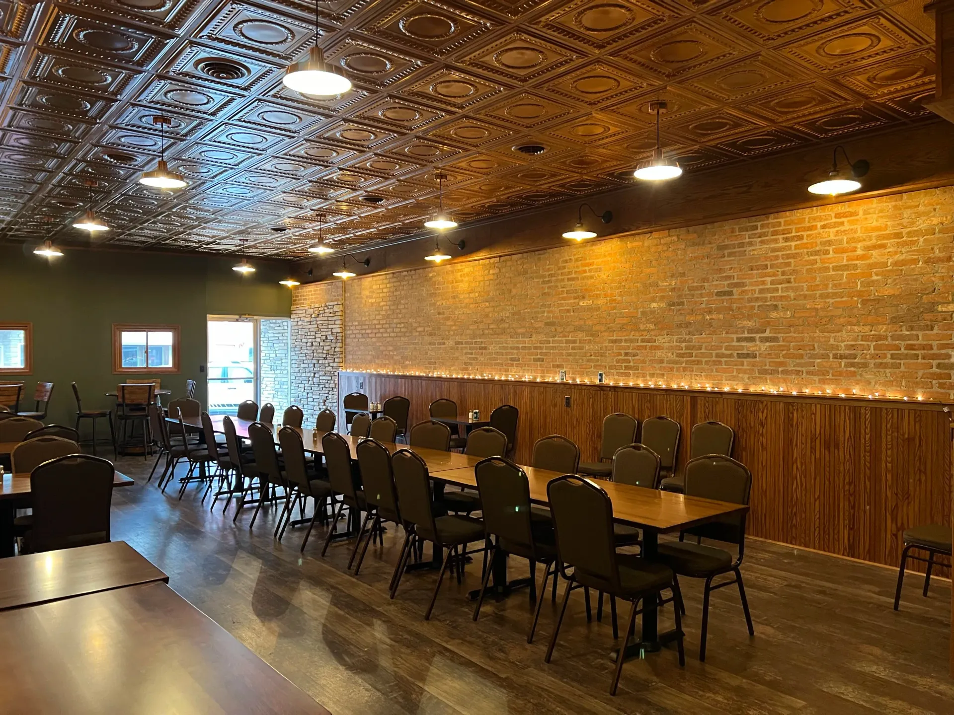 Empty restaurant dining room with rows of chairs, brick walls, and ornate patterned ceiling lights