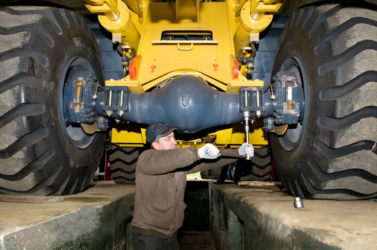 A Man is Working on the Underside of a Large Yellow Truck — North Coast Construction Equipment In Kempsey, NSW
