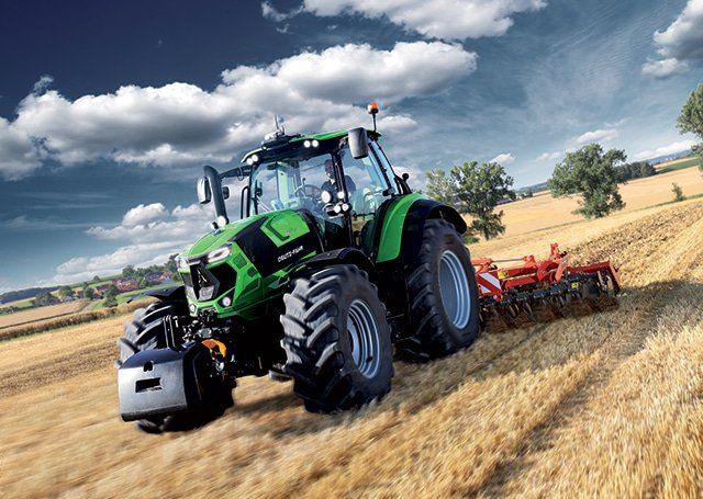 Green tractor working a field under dramatic clouds.
