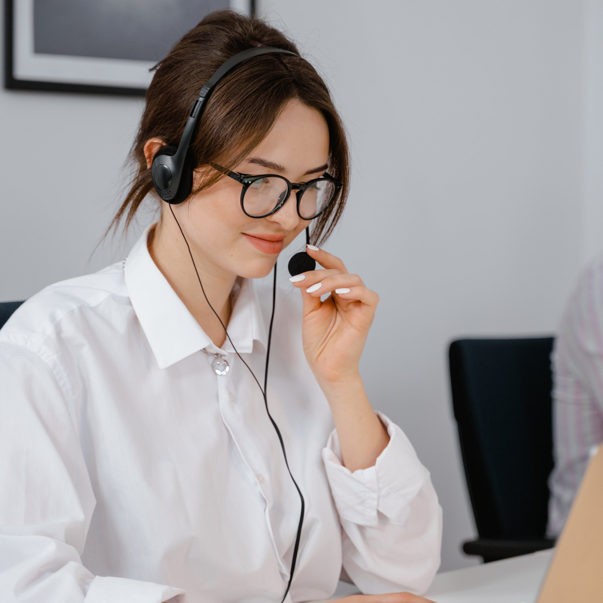 A woman wearing glasses and headphones is sitting in front of a laptop
