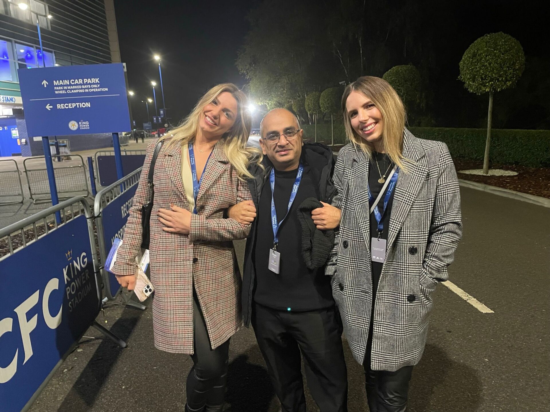 A man and two women are posing for a picture in a parking lot.