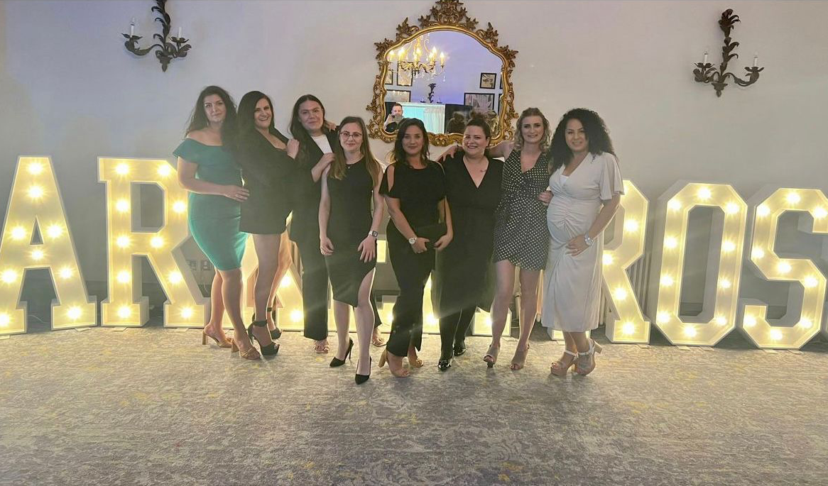 A group of women are posing for a picture in front of a sign that says arros