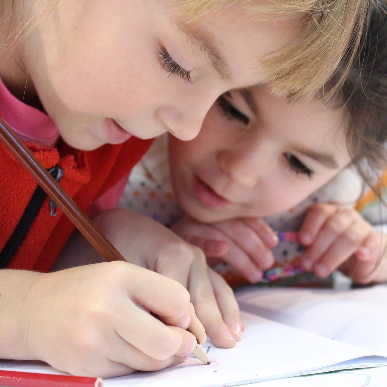 Two young girls are writing on a piece of paper with pencils