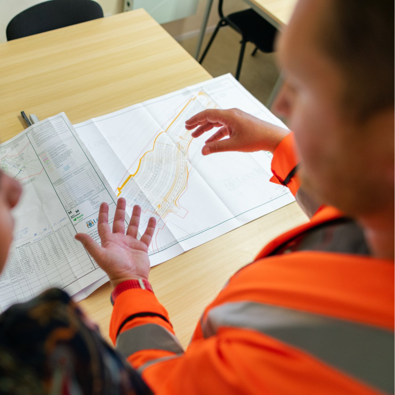 A man in an orange jacket is pointing at a map