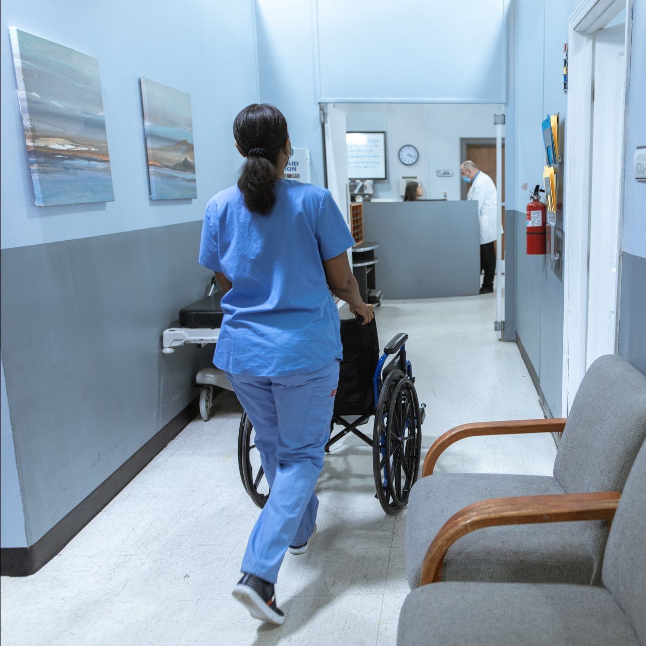 A nurse pushes a wheelchair down a hospital hallway