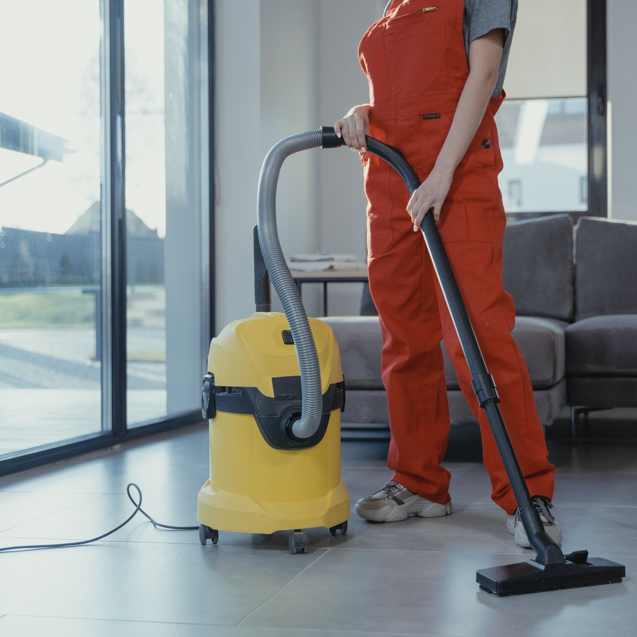 A woman in red overalls is using a yellow vacuum cleaner