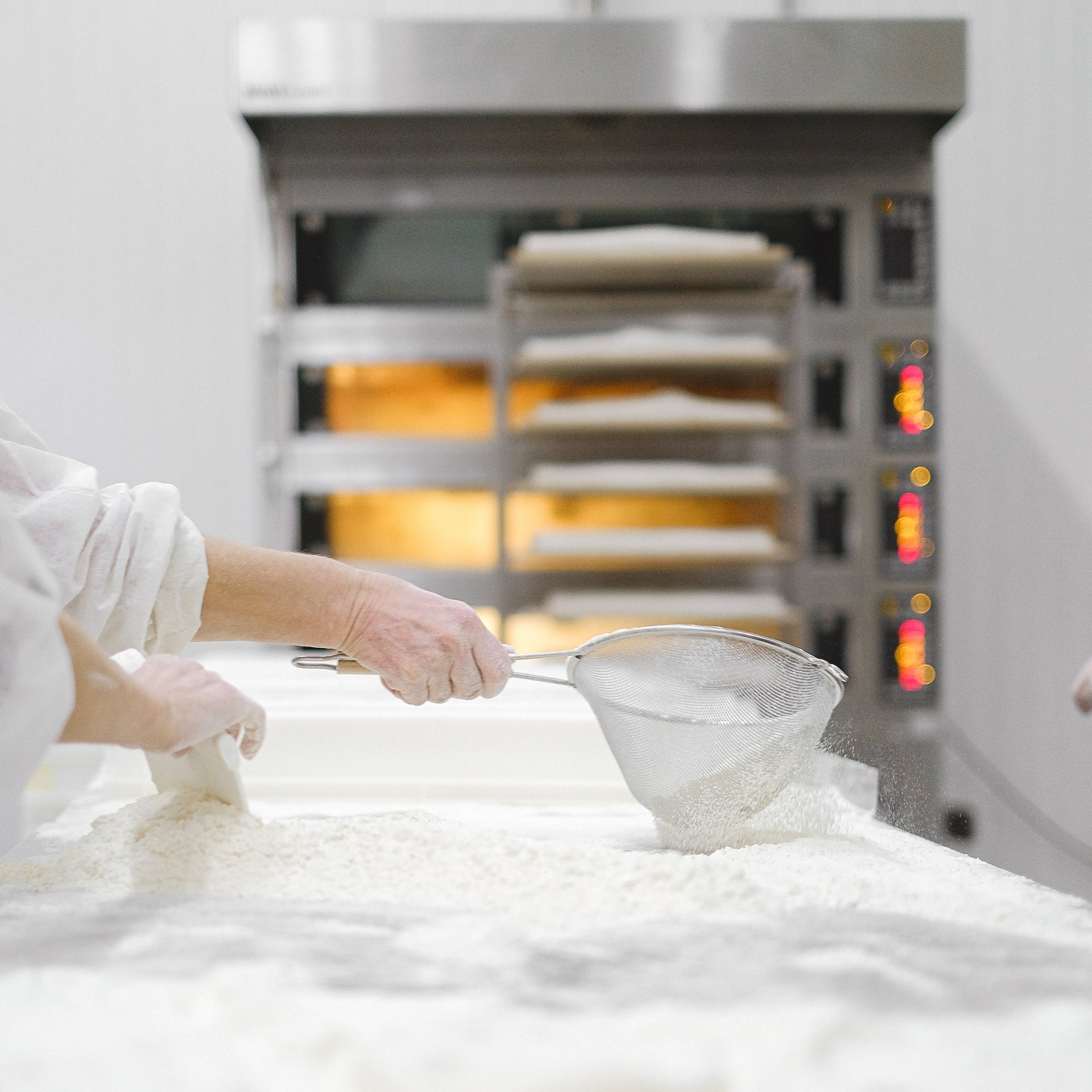 A person is sifting flour on a table in a bakery.