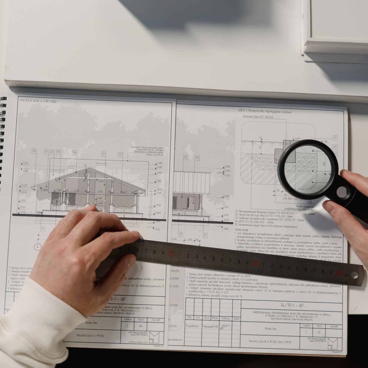 A person is measuring a house with a ruler and magnifying glass