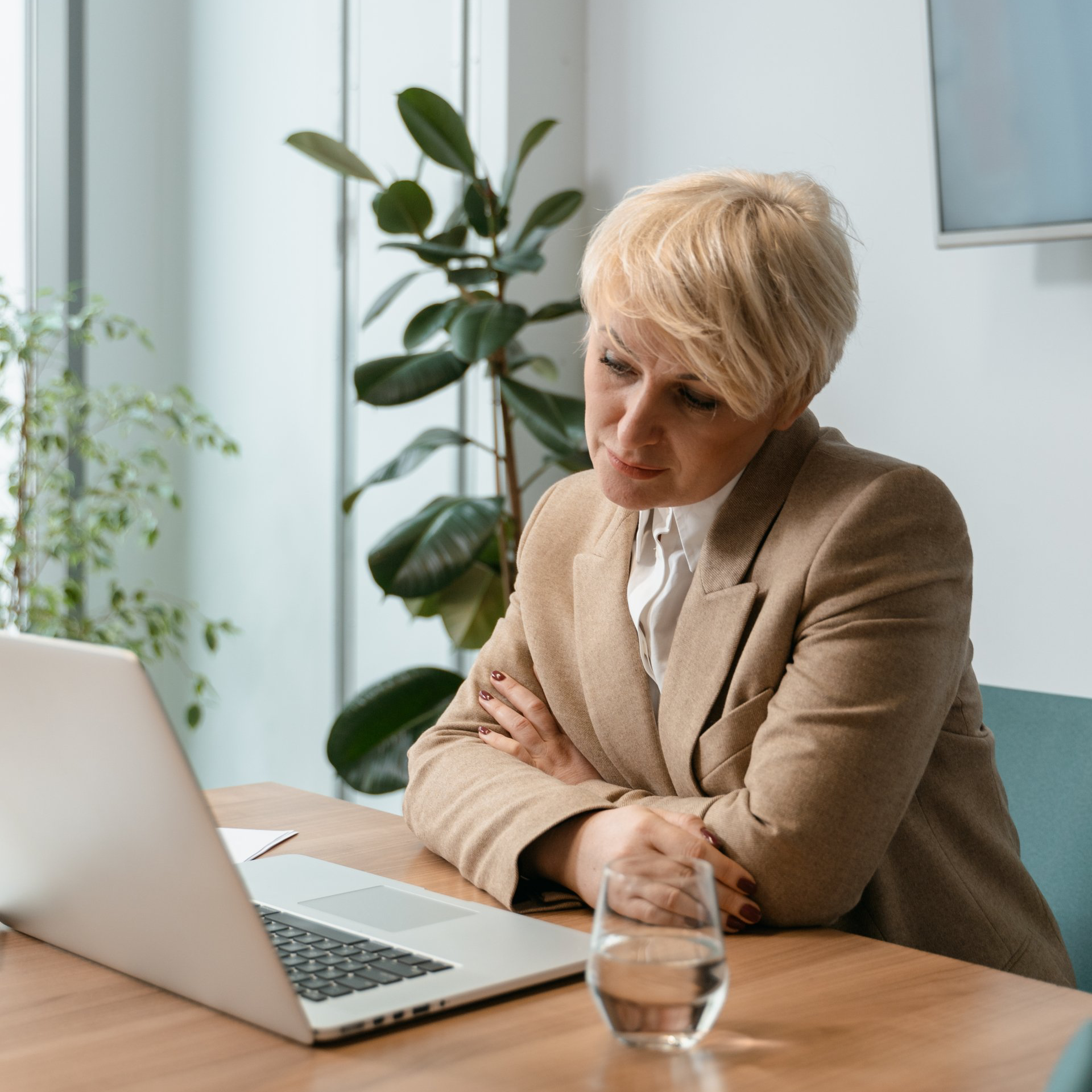 A woman is sitting at a table with a laptop and a glass of water.