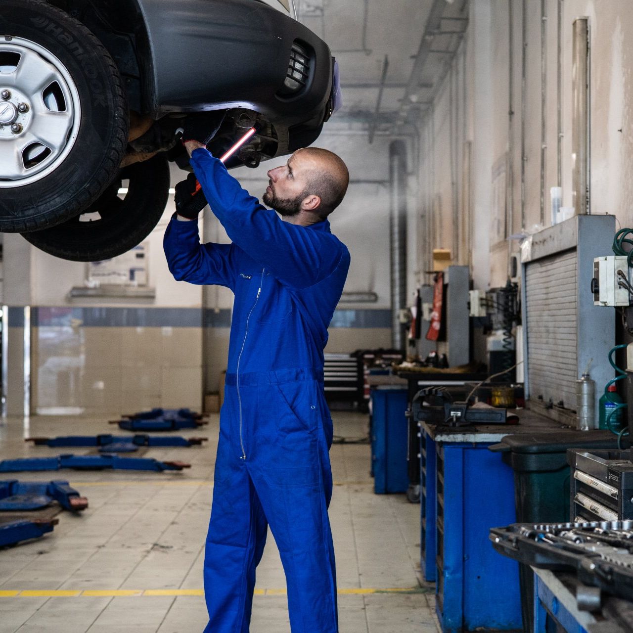 A man in a blue jumpsuit is working under a car