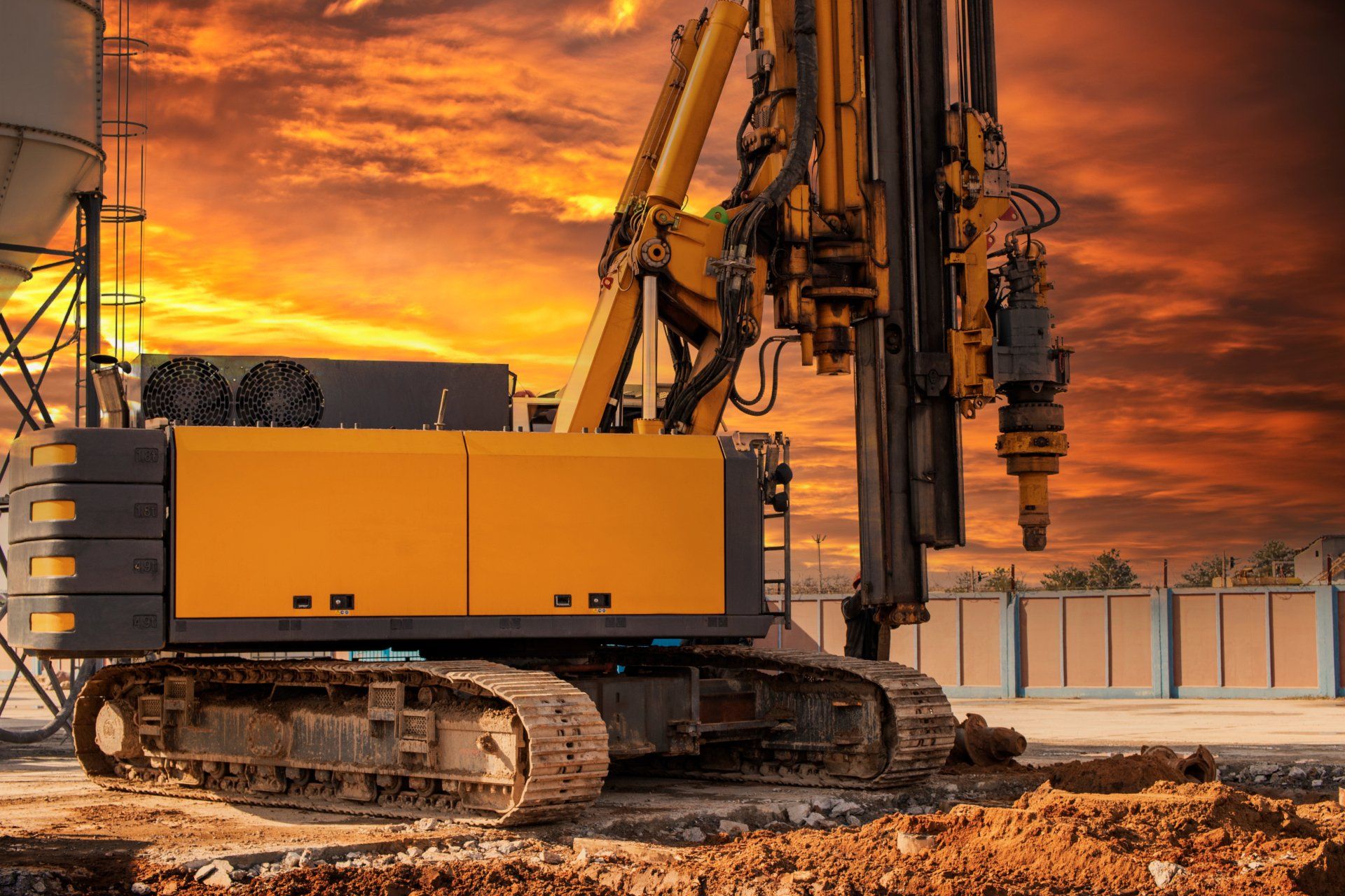 A large yellow excavator is working on a construction site at sunset.