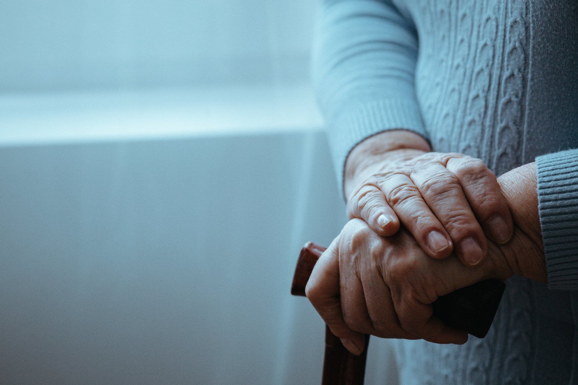 An elderly woman is holding a cane in her hands.