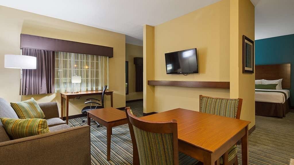 A hotel room with a couch , table , chairs and a flat screen tv.