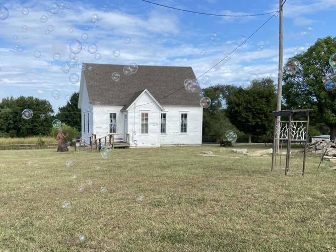 A white house is sitting in the middle of a grassy field surrounded by soap bubbles.