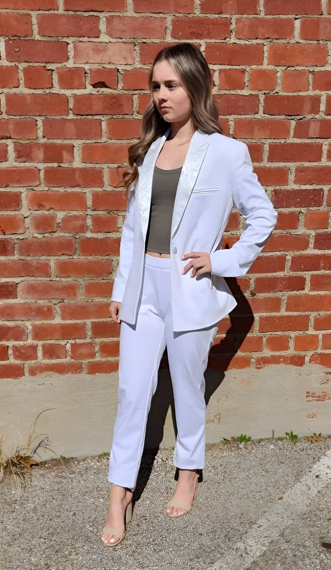 A woman in a white tuxedo is standing in front of a brick wall.