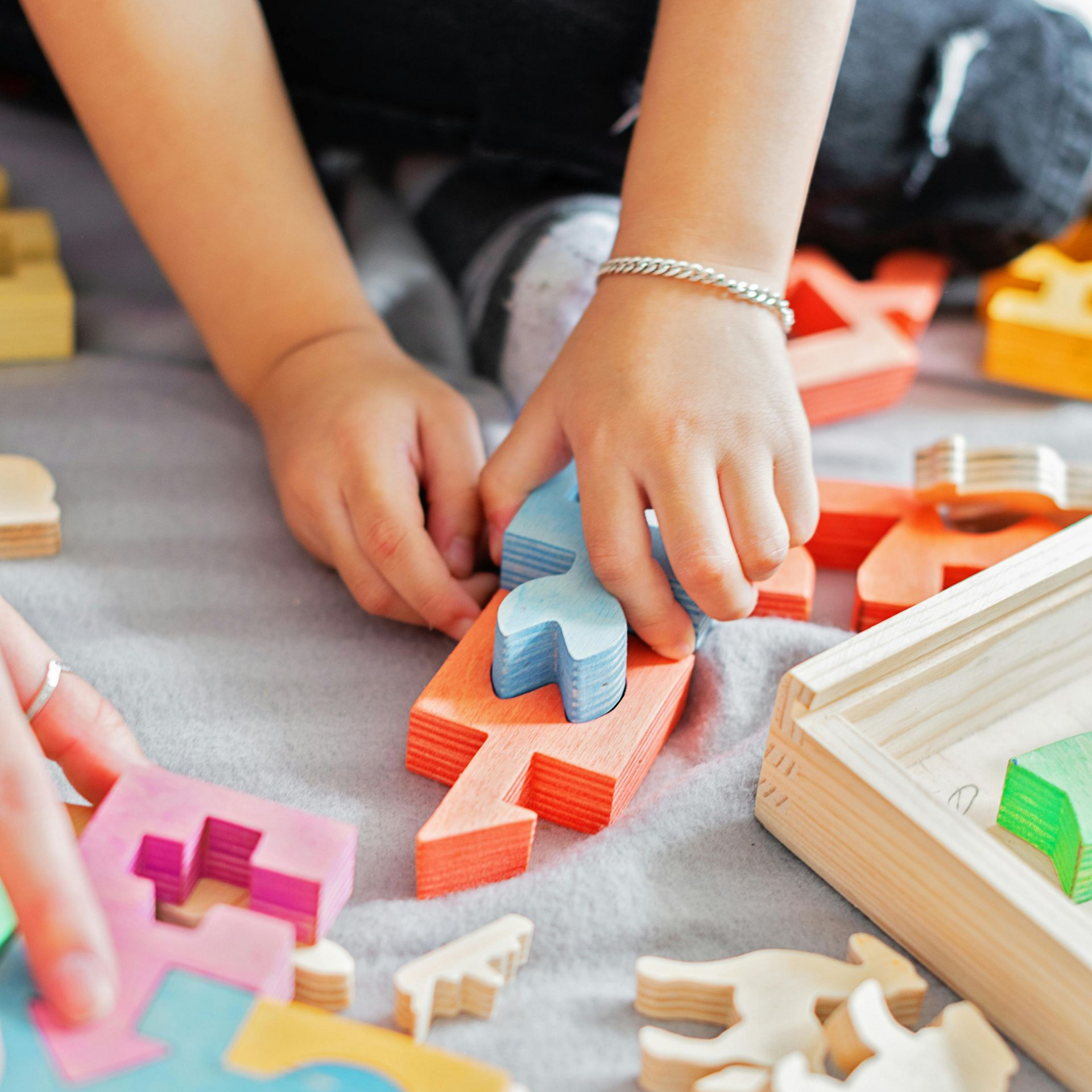 Hands arranging colorful wooden puzzle pieces on a table